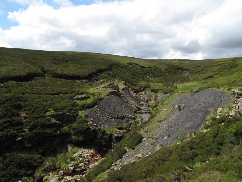 The site of the former Punchard Coal Level in Arkengarthdale, showing an eroding spoil heap and ruined building; the mine portal itself is no longer visible.