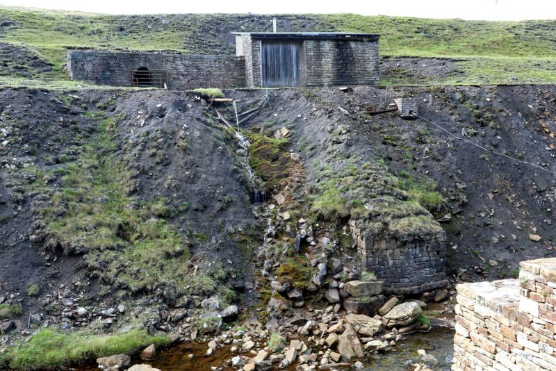 A small stone building beside a moorland river, standing next to the mine's adit entrance.