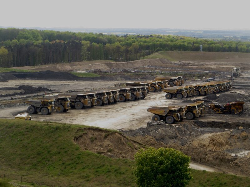 Rows of large yellow dump trucks parked in lines on the bare ground of the opencast site