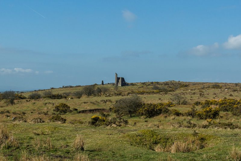 Rough moorland with gorse and shallow hollows, and a ruined engine house and chimney on the skyline.