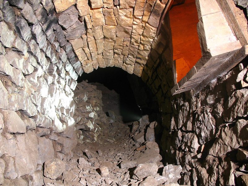 A timber and stone ore hopper standing in an underground chamber lit by a lamp.