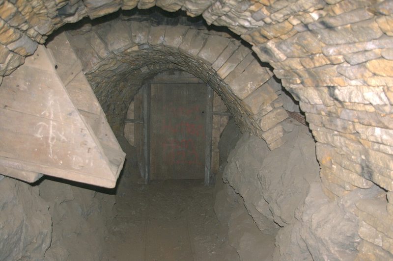 A timber ventilation door set across a narrow underground passage beside an ore hopper.