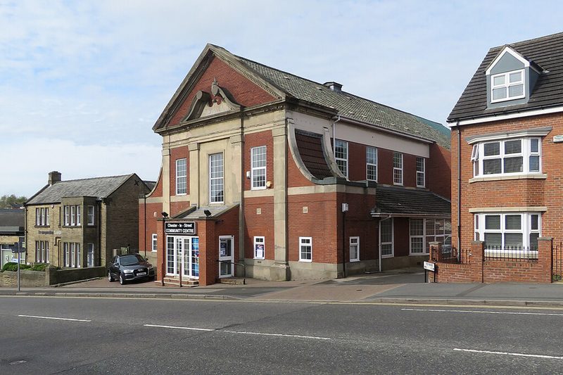 A two-storey red-brick and stone hall with a pedimented gable, signed as Chester-le-Street Community Centre, beside a road.