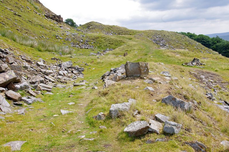 A grassy level track running between spoil heaps of broken grey sandstone slabs on the fell side, 2022