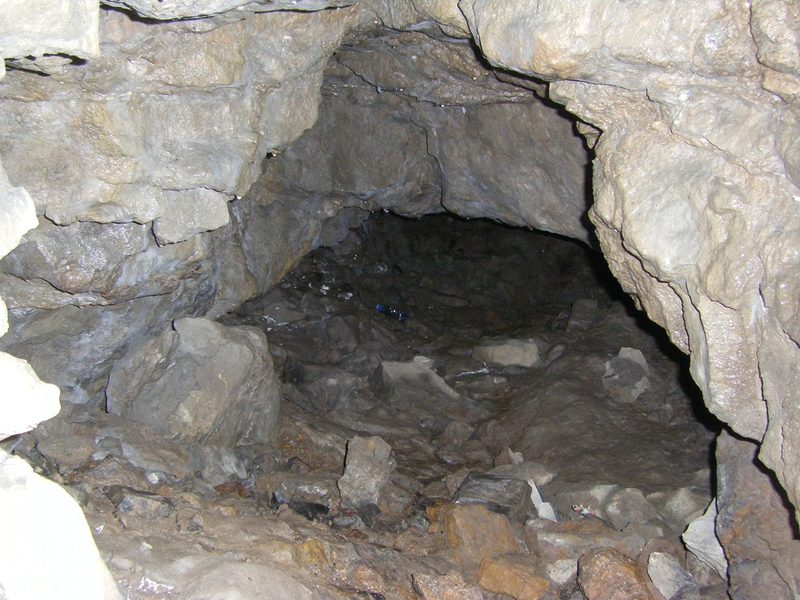 A low rocky passage in pale limestone with loose stones and rubble on its floor, fading into darkness.