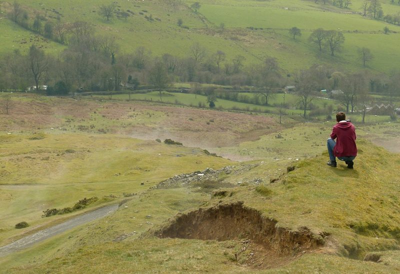 A disused dhustone quarry on Titterstone Clee, dark rock faces above a floor of broken stone, with a photographer for scale.