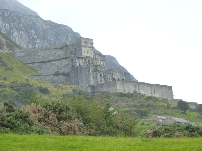 Roofless stone and concrete quarry buildings on a steep hillside below rock galleries