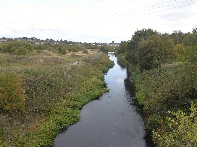 The straightened River Dearne running between wooded banks past the site of the former Wath Main Colliery, with housing on the skyline.