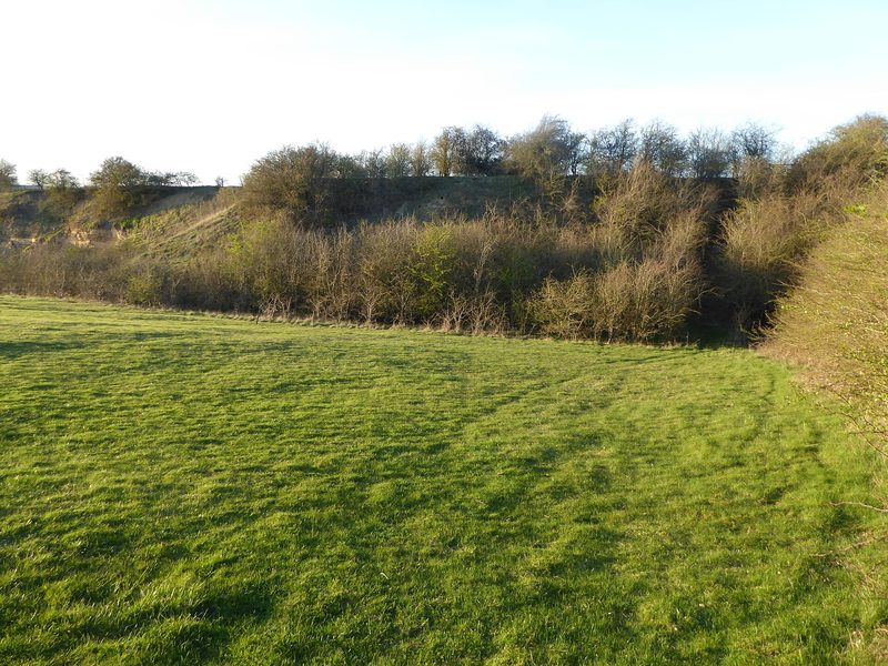 A disused ironstone quarry face east of Wellingborough, now a geological Site of Special Scientific Interest, with grassed slopes below an exposed section.