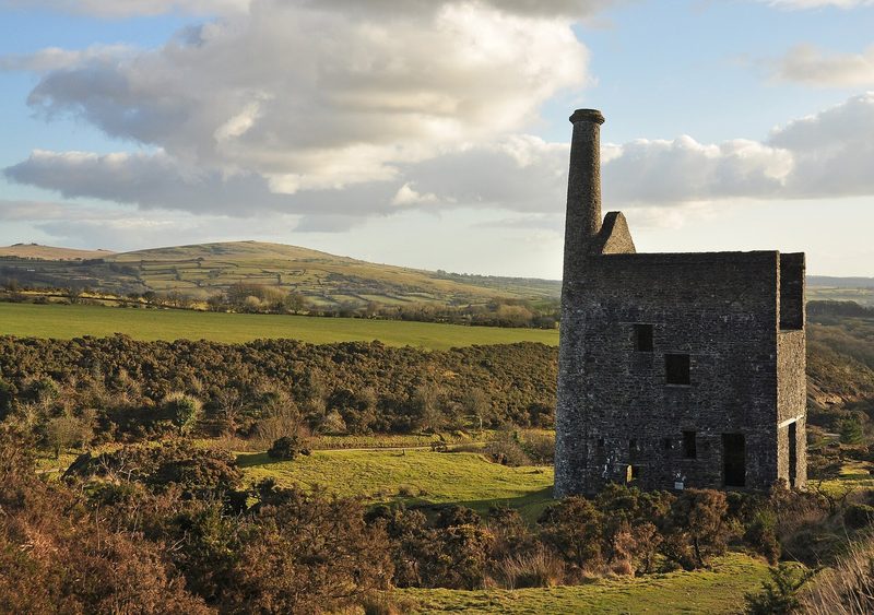 The ruined granite engine house of Wheal Betsy standing on open moorland on the western edge of Dartmoor, with the rounded summit of Cox Tor in the distance under a clear sky