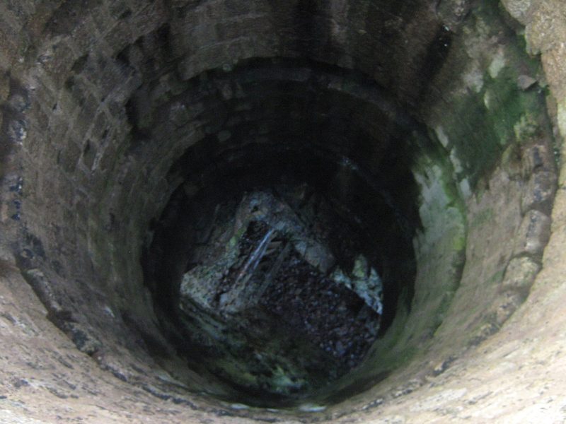 View down the stone-lined main pumping shaft of Wheal Cock through its protective grille.