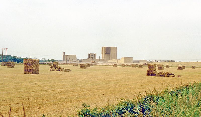 The pale clad headframe tower and low surface buildings of Whitemoor Mine seen across a hayfield of stacked bales in 1988