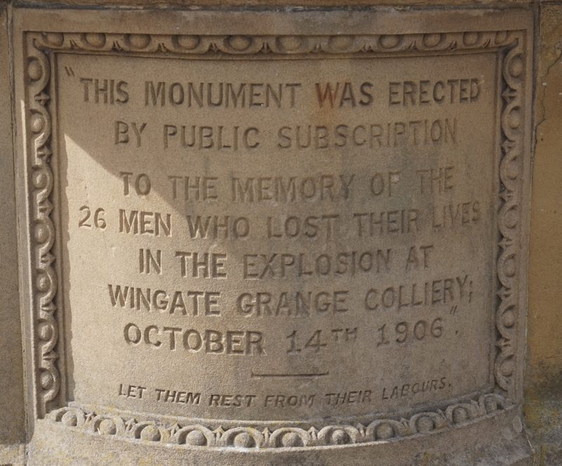 A carved sandstone panel reading 'This monument was erected by public subscription to the memory of the 26 men who lost their lives in the explosion at Wingate Grange Colliery, October 14th 1906'