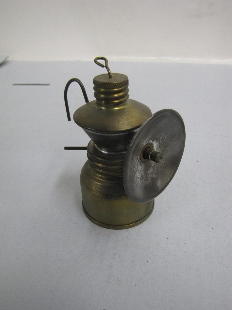 A brass carbide acetylene cap lamp with a curved hanging hook and a polished reflector disc.