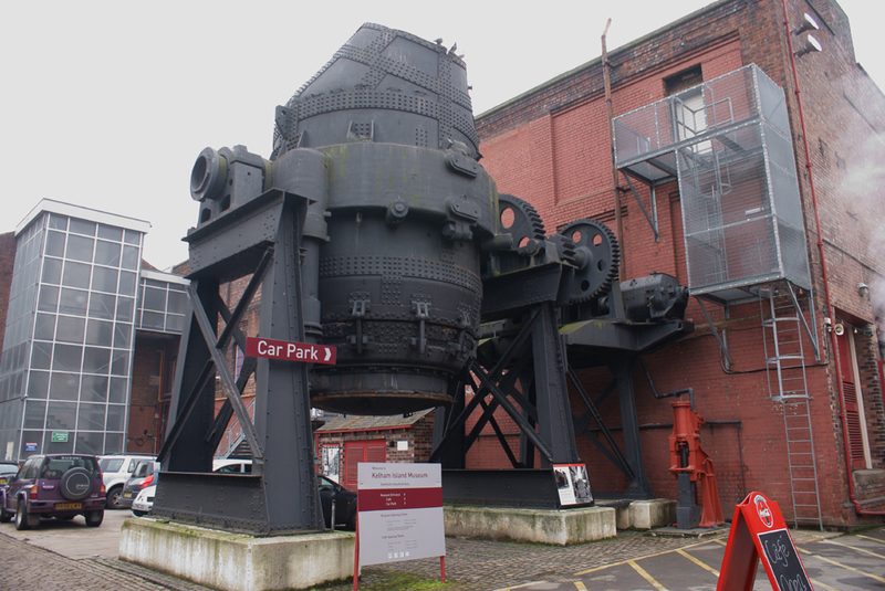 A large pear-shaped steel converter vessel tilted on its side on a mounting outside a museum building.