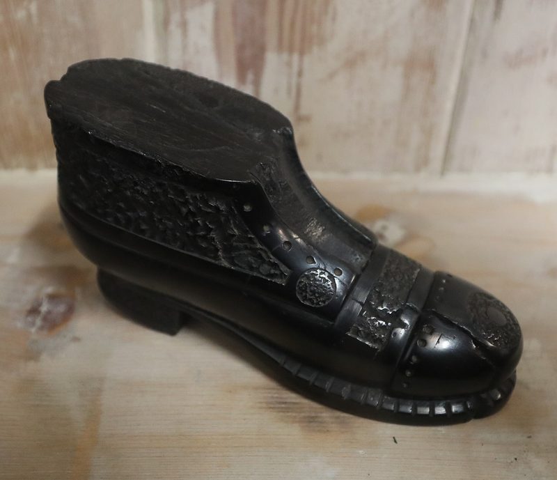 A polished black sculpture of a laced boot carved from a single block of cannel coal, displayed at the Black Country Living Museum