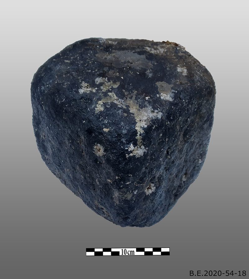 A heavily worn, rounded dark lump of coal roughly the size of two fists, its original rectangular block shape eroded away by decades underwater, photographed against a grey background with a 10cm scale bar.