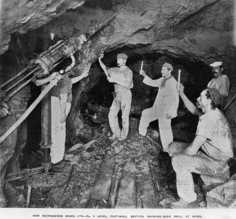 A miner operating a pneumatic rock drill underground at the New Ravenswood Mines, Queensland, around 1905 -- captioned in the original as showing a rock drill at work on the No. 4 Level foot-wall.